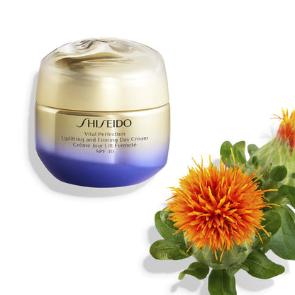 Shiseido Vital Perfection Day Cream in a gold and blue jar next to an orange flower with green leaves